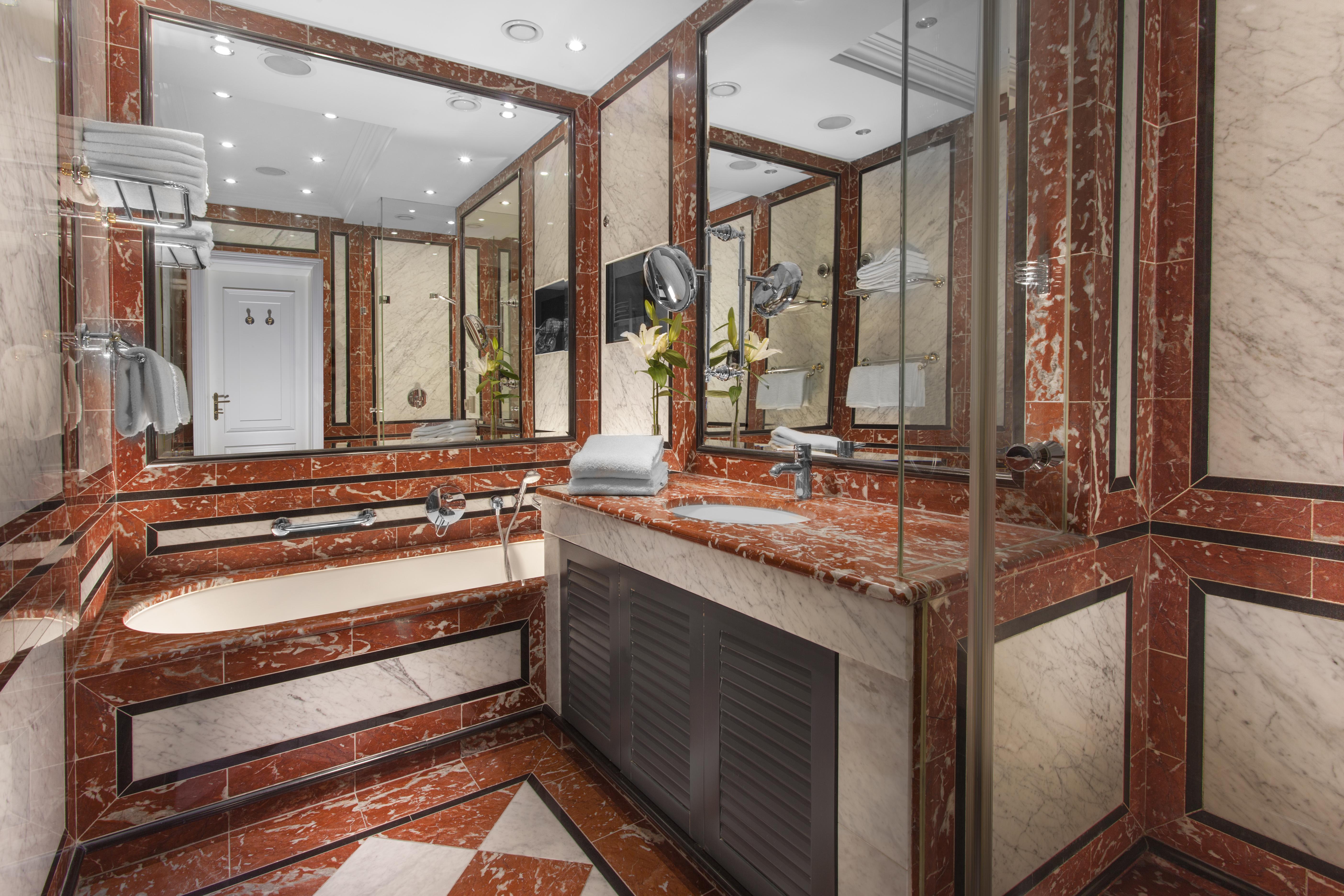 Art Nouveau Palace Hotel Praha Bagian luar foto The photo shows a luxurious bathroom featuring a combination of marble finishes in warm tones, including red and cream. There is a bathtub integrated into the design, along with a sink area that has a large countertop. The walls are adorned with mirr