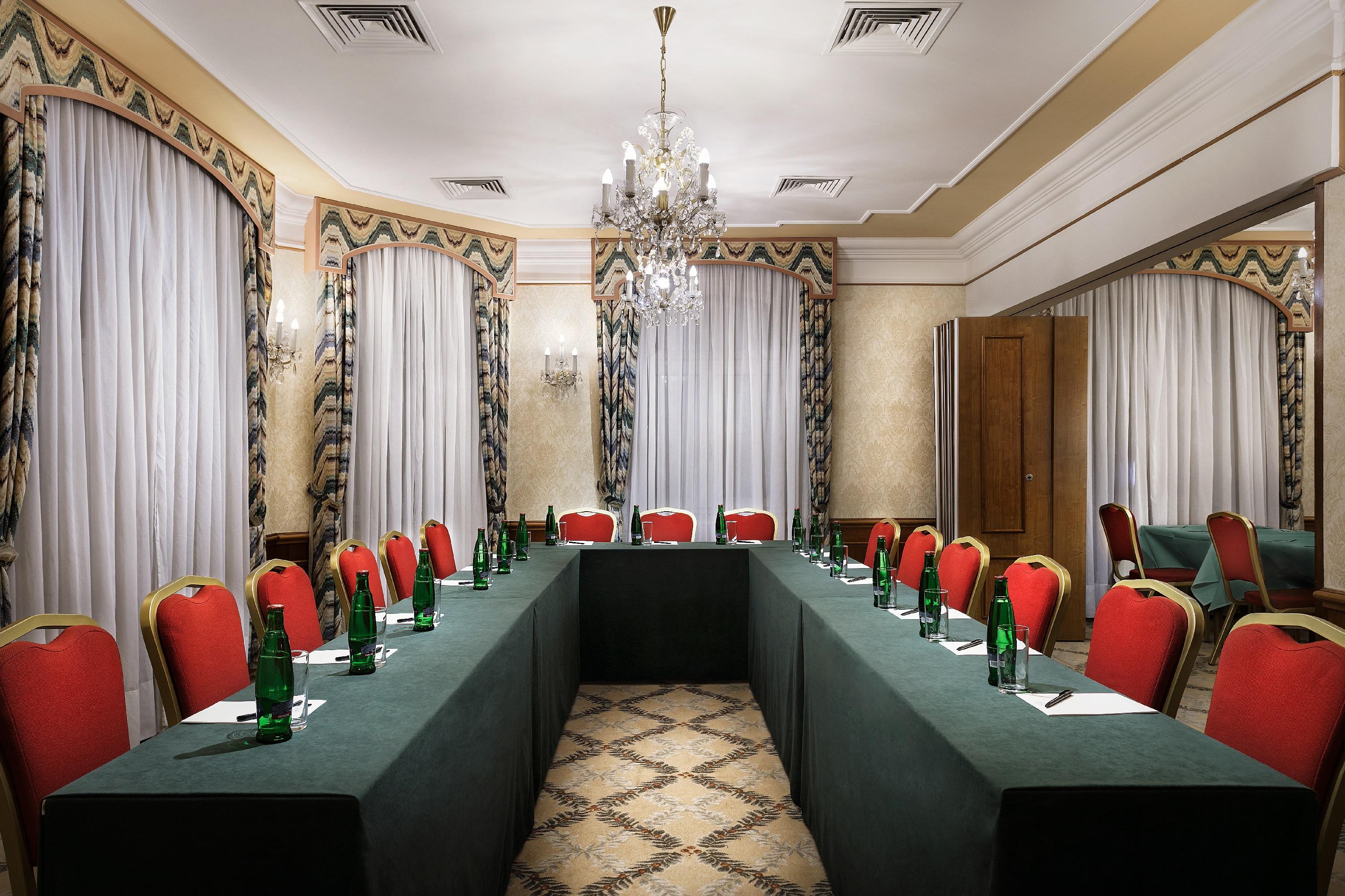 Art Nouveau Palace Hotel Praha Bagian luar foto The photo shows a conference room set up for a meeting. There is a rectangular arrangement of tables covered with green cloth, surrounded by red chairs. Each place has a notebook and an unfinished glass bottle of water. The room features elegant deco