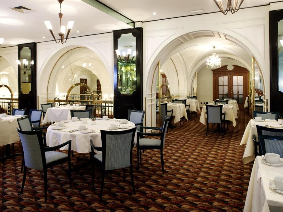 Art Nouveau Palace Hotel Praha Bagian luar foto The photo shows an elegant restaurant interior. It features a spacious layout with several dining tables, each set with white tablecloths and dining ware. The room has a sophisticated ambiance, highlighted by architectural arches and decorative mirro