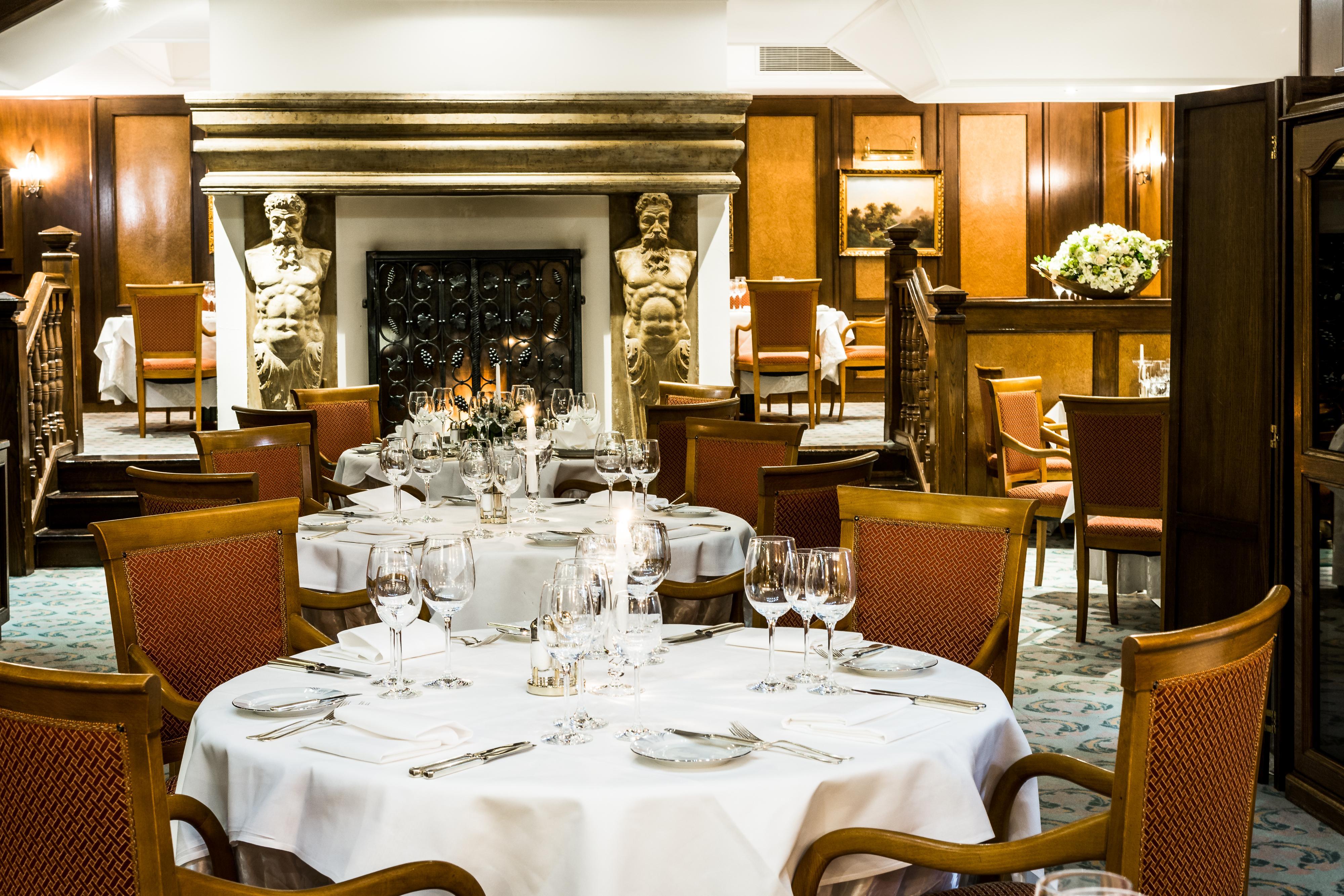Art Nouveau Palace Hotel Praha Bagian luar foto The photo shows an elegant restaurant interior. There is a round dining table set with white tablecloths, fine cutlery, and glassware. In the background, a cozy fireplace is flanked by decorative statues. The decor features rich wooden paneling and w