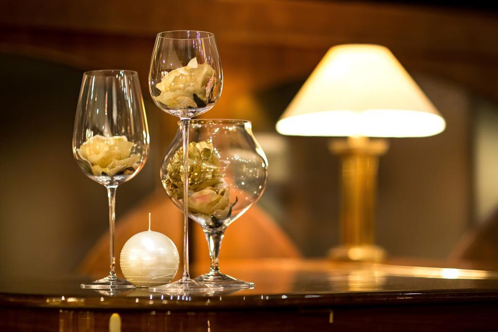 Art Nouveau Palace Hotel Praha Bagian luar foto The photo features a decorative arrangement with three wine glasses, each containing different floral elements, including roses. There is also a round white candle positioned on the surface alongside the glasses. In the background, a lamp emits a sof