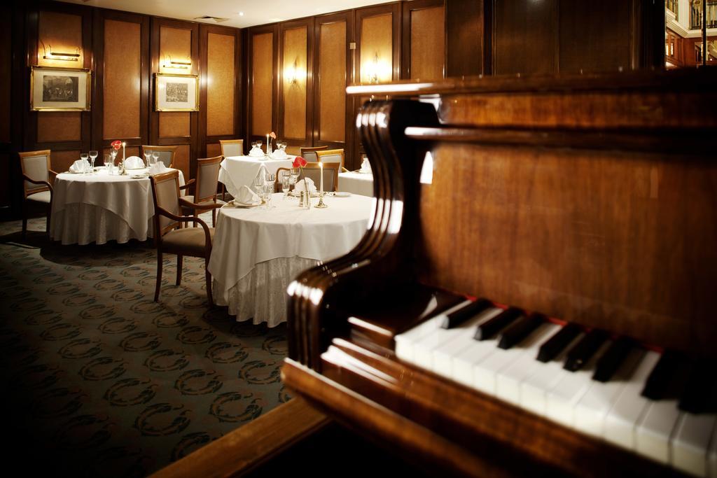 Art Nouveau Palace Hotel Praha Bagian luar foto The photo shows an elegant dining room with a classic ambiance. In the foreground, there is a wooden piano, partially in view, which adds to the sophisticated atmosphere. The tables are set with white tablecloths, fine dining ware, and flowers, sugge
