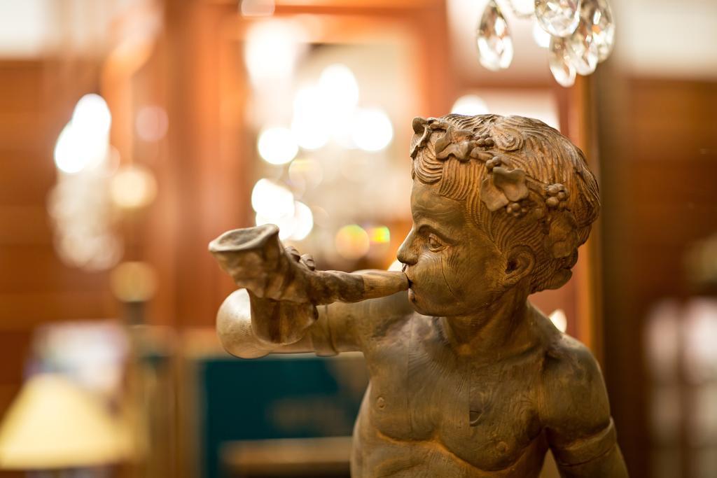 Art Nouveau Palace Hotel Praha Bagian luar foto The image shows a bronze sculpture of a young boy who appears to be playing a musical instrument, likely a flute or horn. The boy is depicted in a realistic style, with details such as his facial expression and hair. The background appears blurred, f